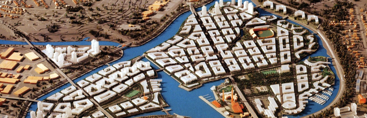 Scale model of a town at the fork of a river used in a landscape architect's community planning session. There is bright blue river water and rows of white buildings cover a peninsula.