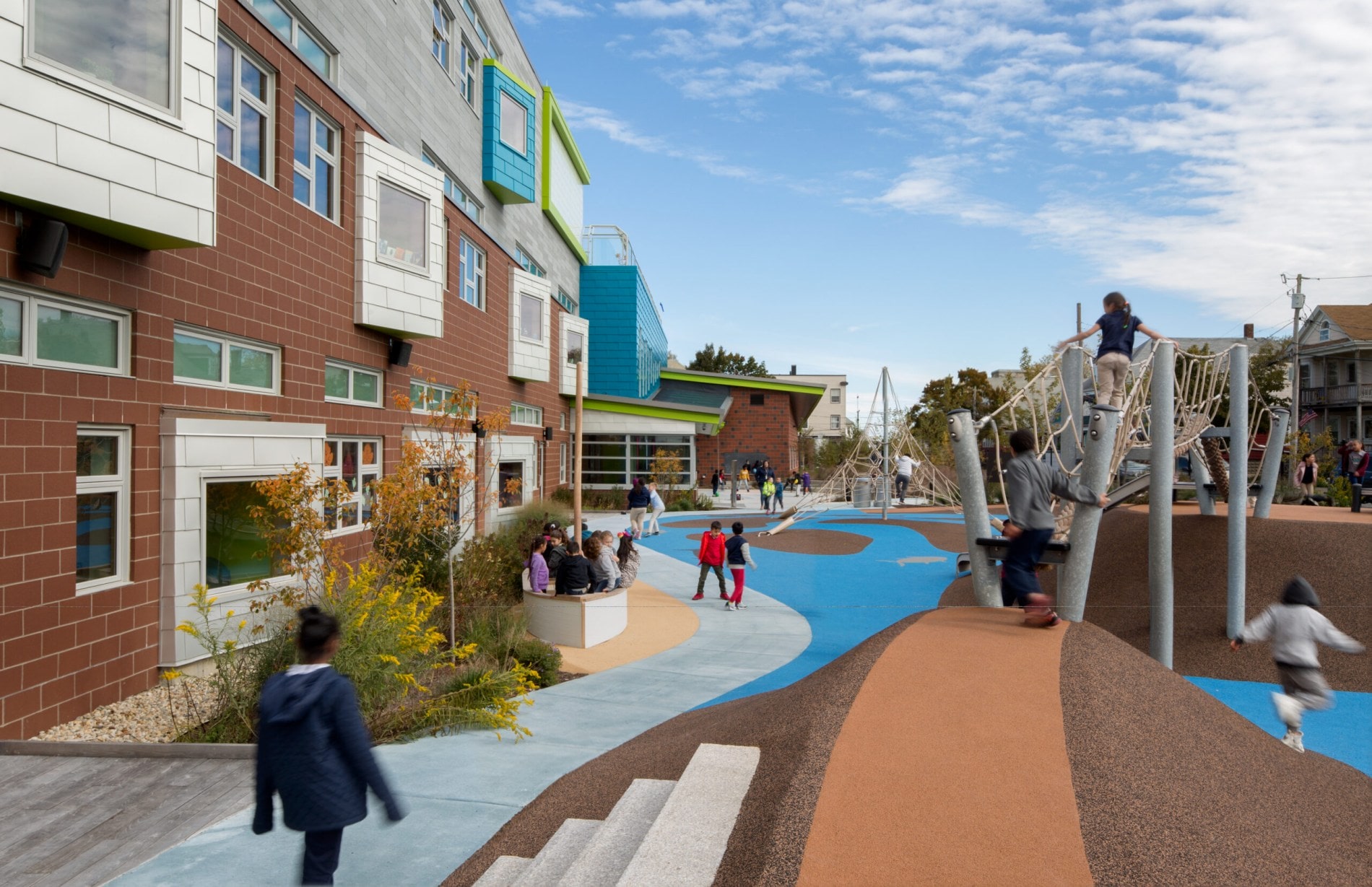 Students are seen running around a new ocean-themed adventure playground outside of Jacobs Elementary school, including a rope bridge over a blue rubberized safety surface that looks like a river running between islands.